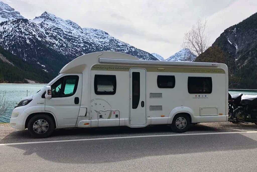 A motorhome over 3.5 tonnes, sitting in front of a beautiful lake with snow encrusted mountains in the background.  